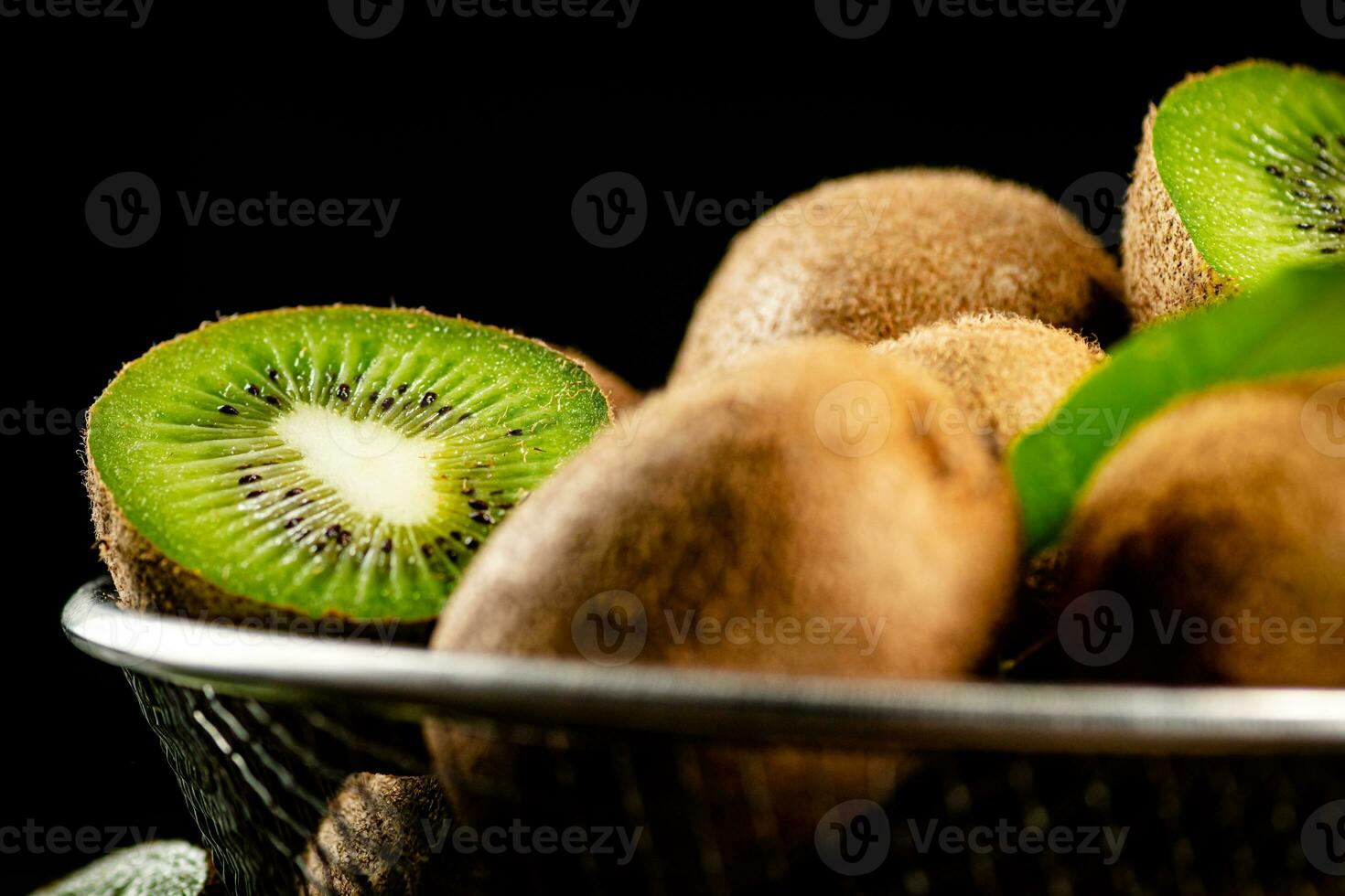 Ripe kiwi with leaves in a colander on the table. photo