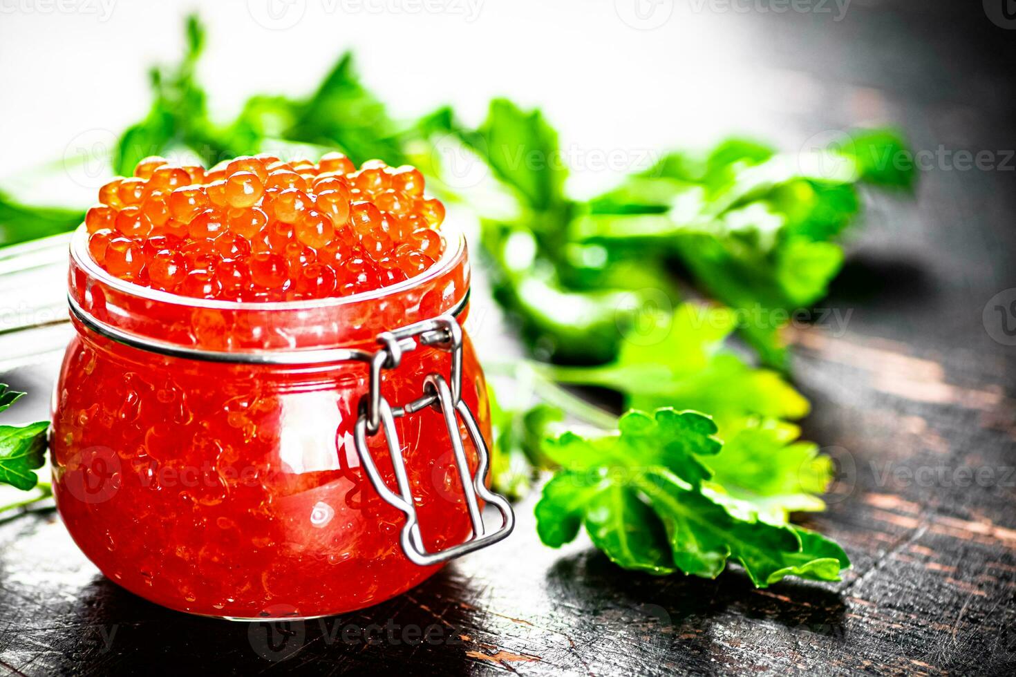 A full jar of red caviar with parsley on the table. photo