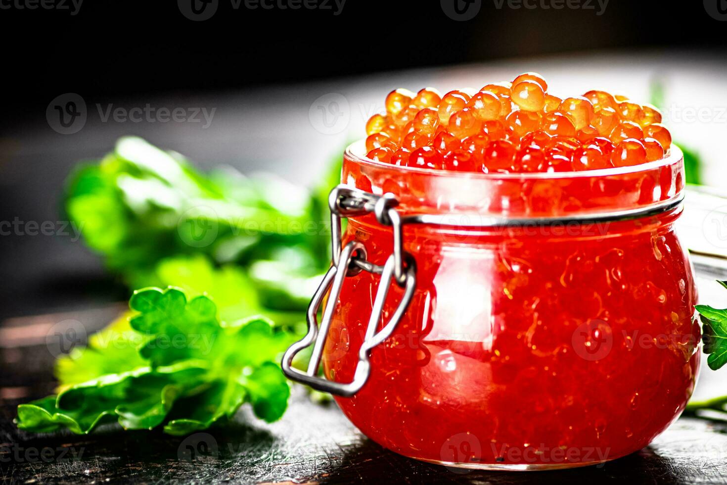 A full jar of red caviar with parsley on the table. photo