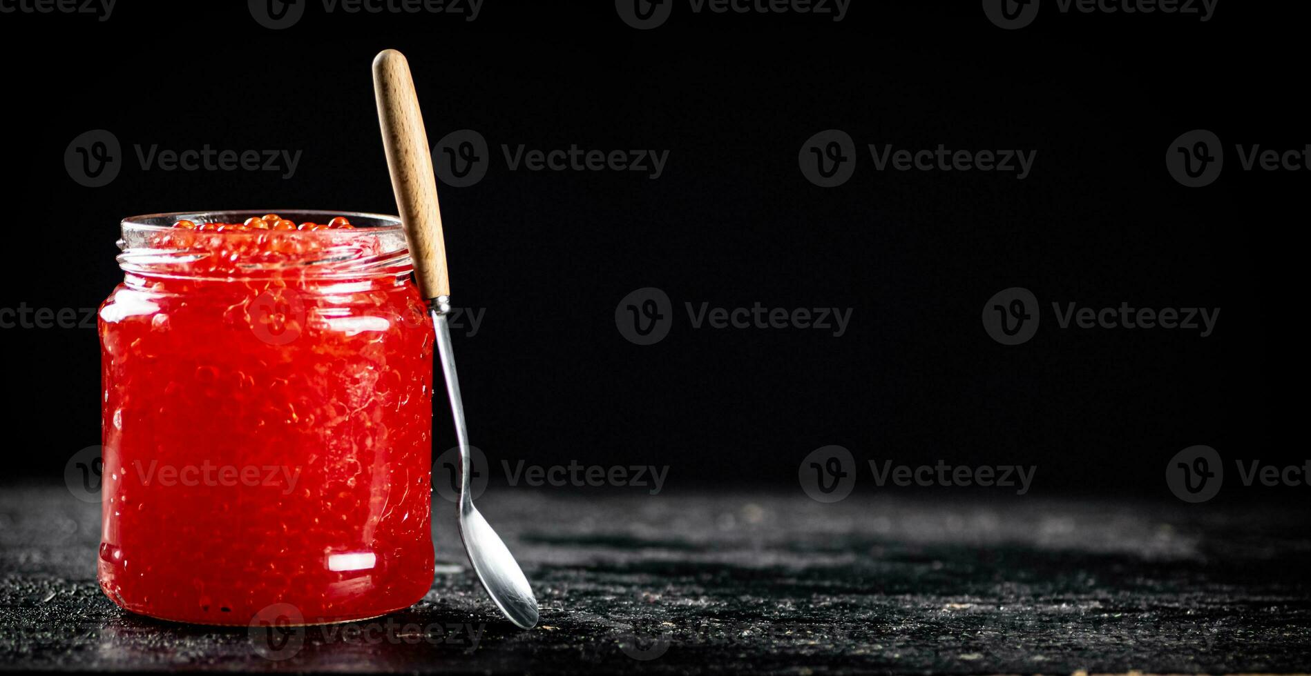 Red caviar in a glass jar on a table with a spoon. photo