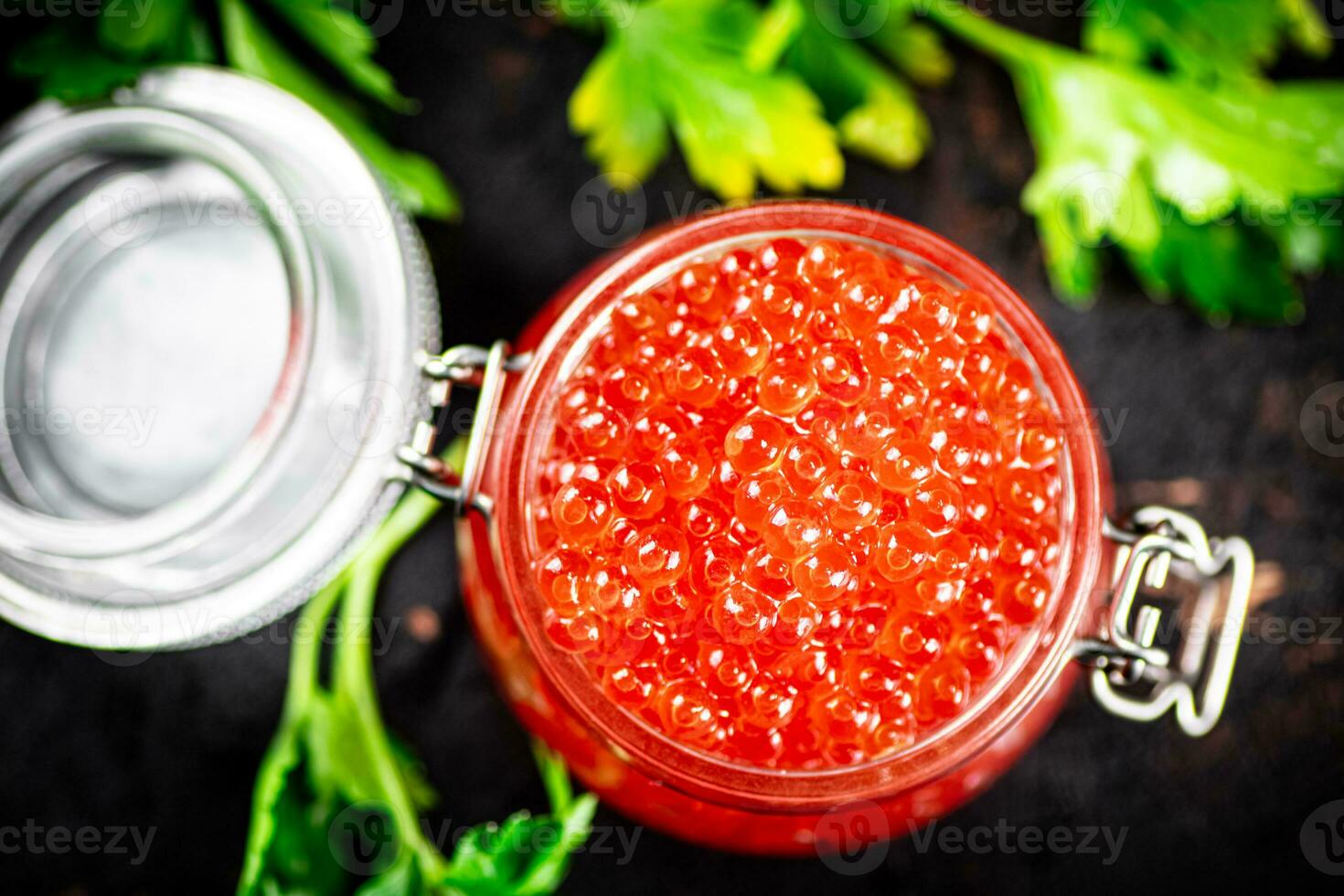 A full jar of red caviar with parsley on the table. photo