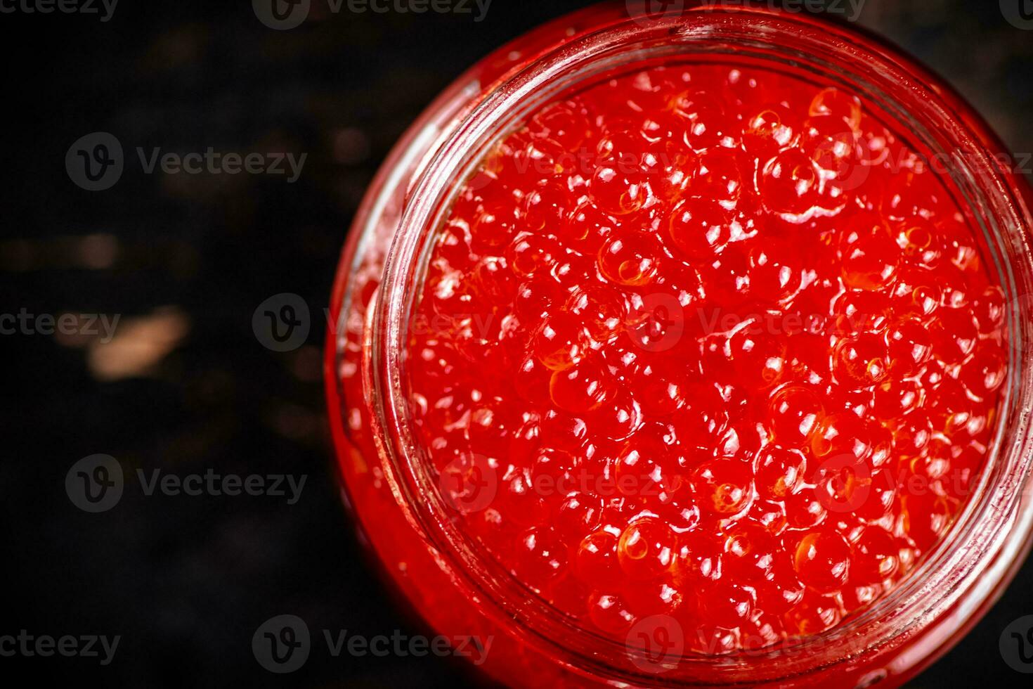 Red caviar in a glass jar. Against a dark background. photo