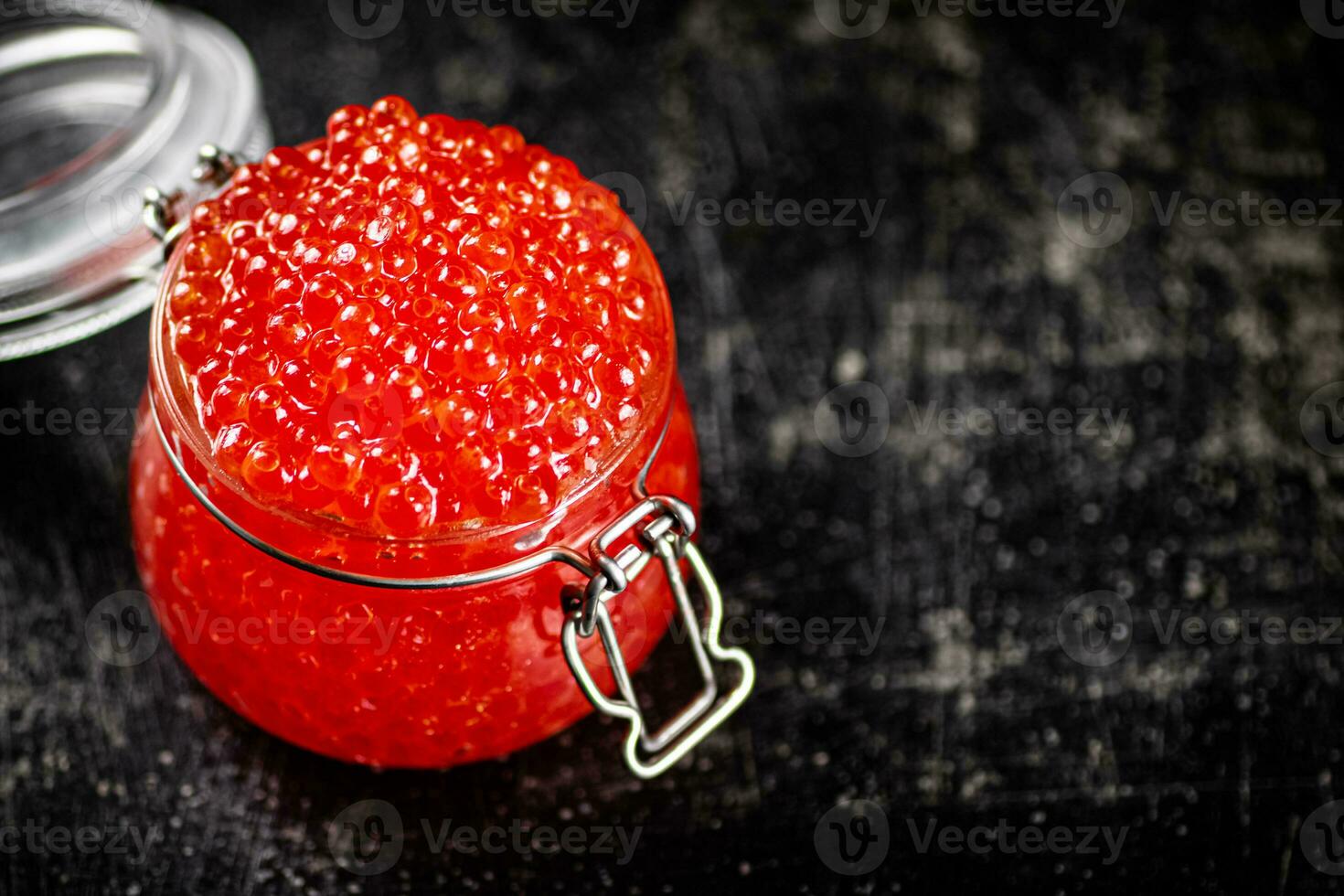 An open glass jar with red caviar on the table. photo