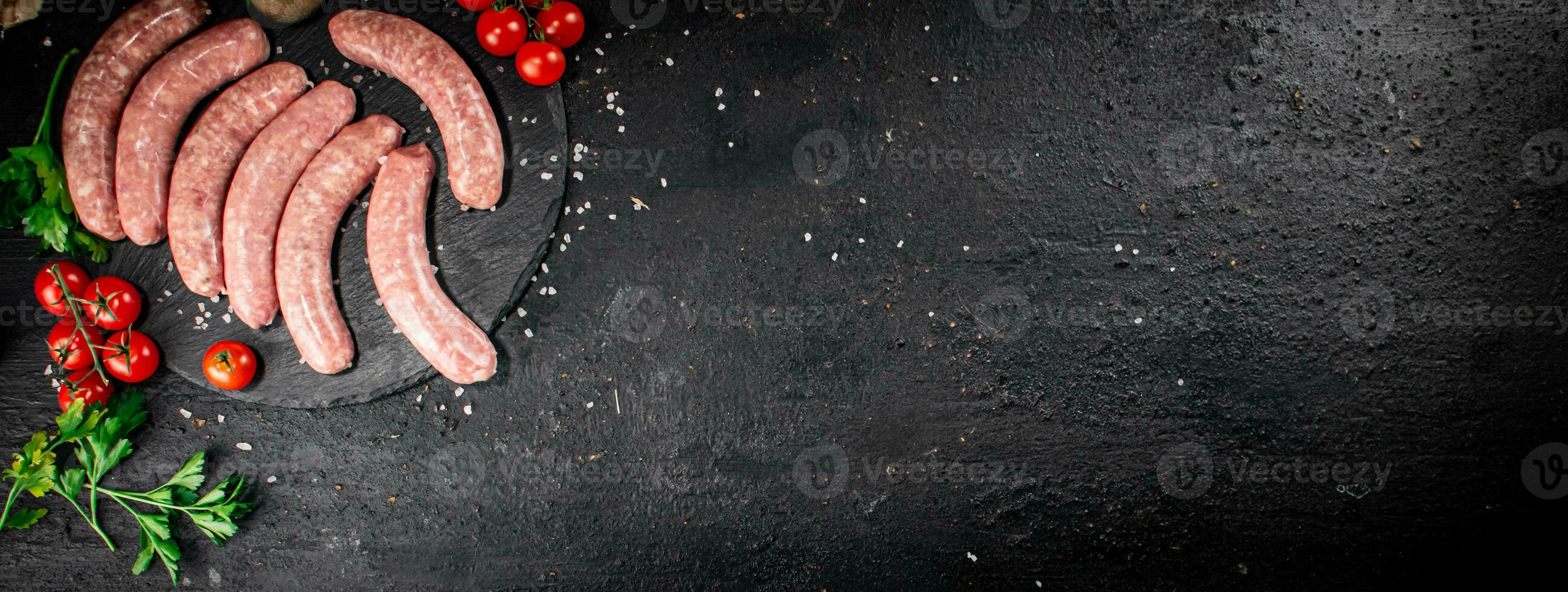 Raw sausages on a stone board with spices, tomatoes and herbs. photo