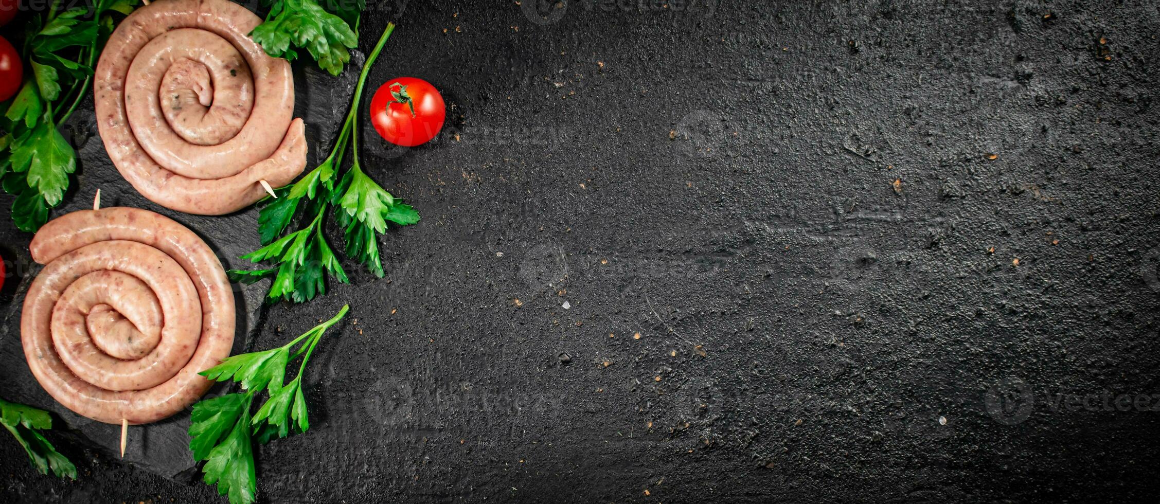 Raw sausages on a stone board with parsley and tomatoes. photo