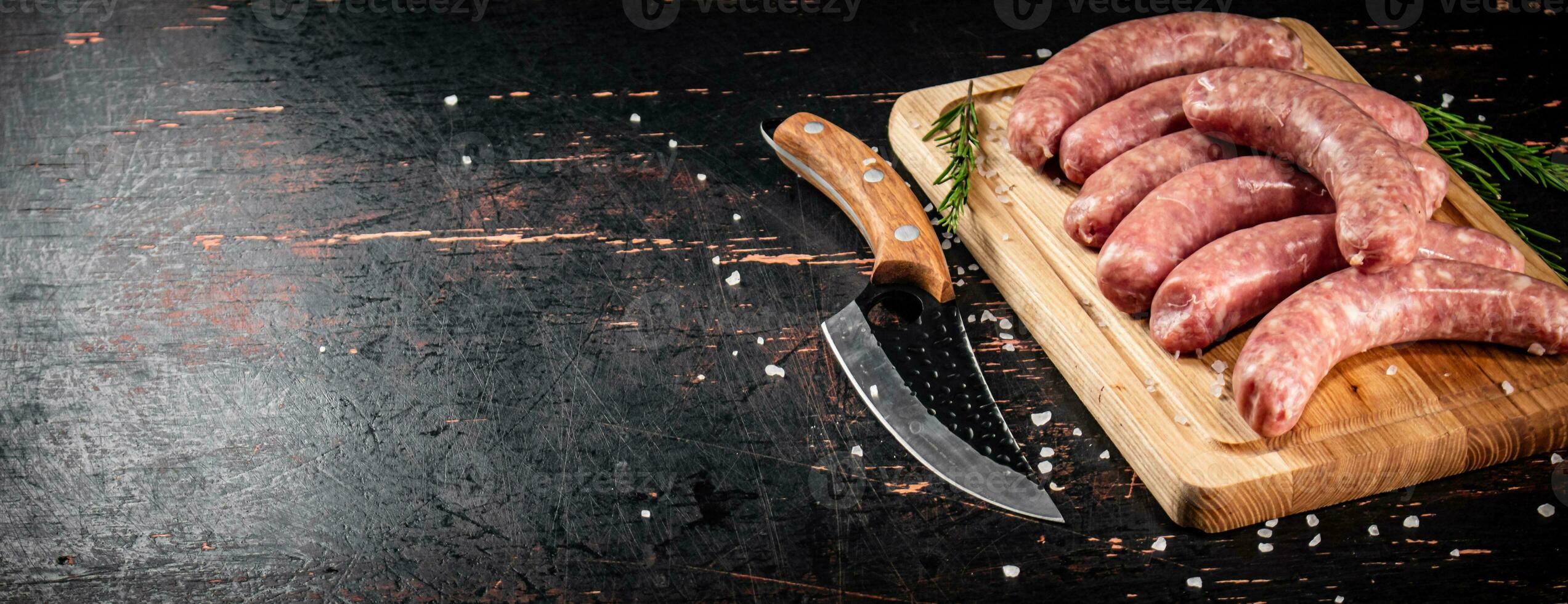 Raw sausages on a cutting board with a knife and rosemary. photo