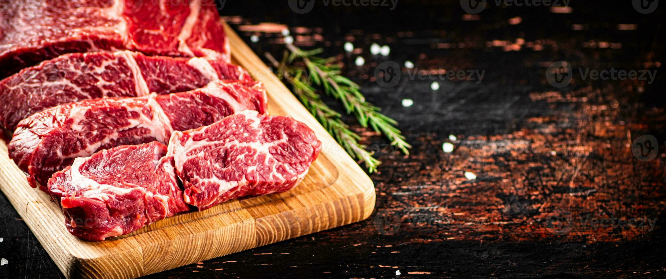 Raw beef on a wooden cutting board with rosemary. photo