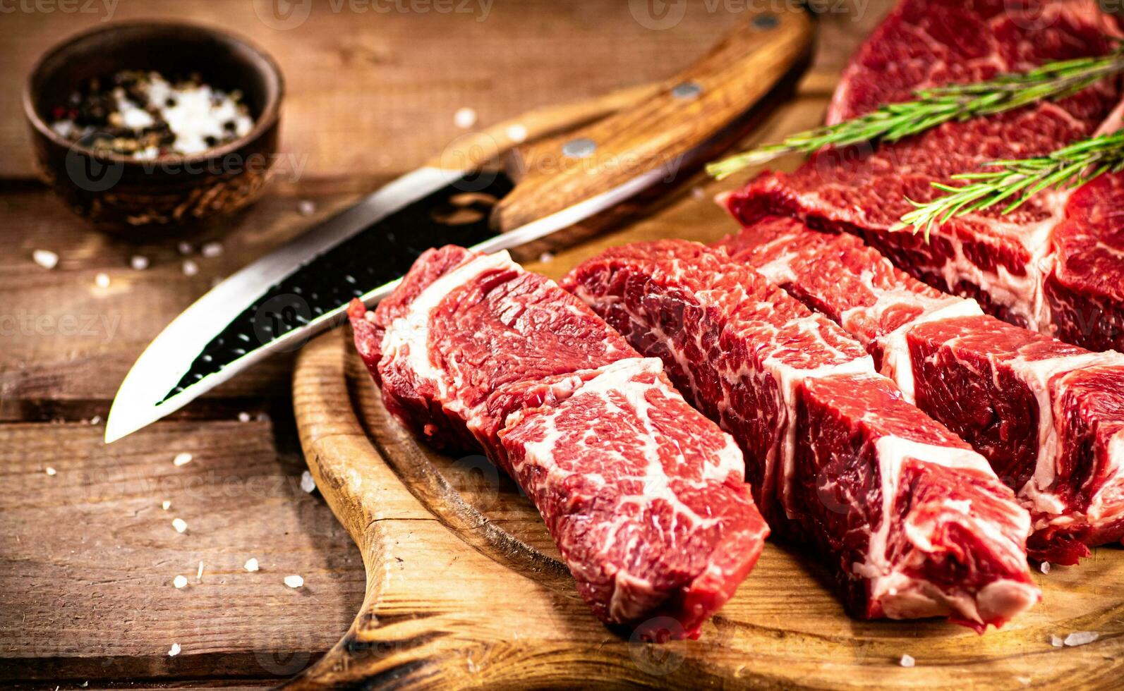 Raw beef on a cutting board with rosemary and spices. photo
