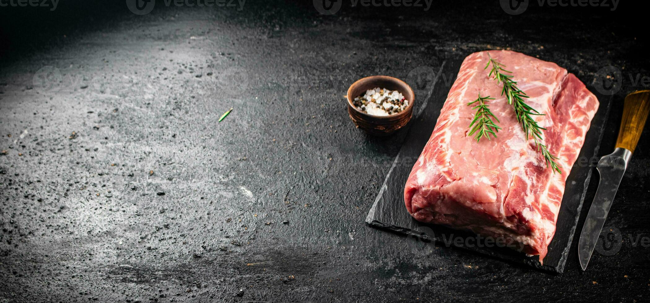 A piece of raw pork on a stone board with a sprig of rosemary. photo