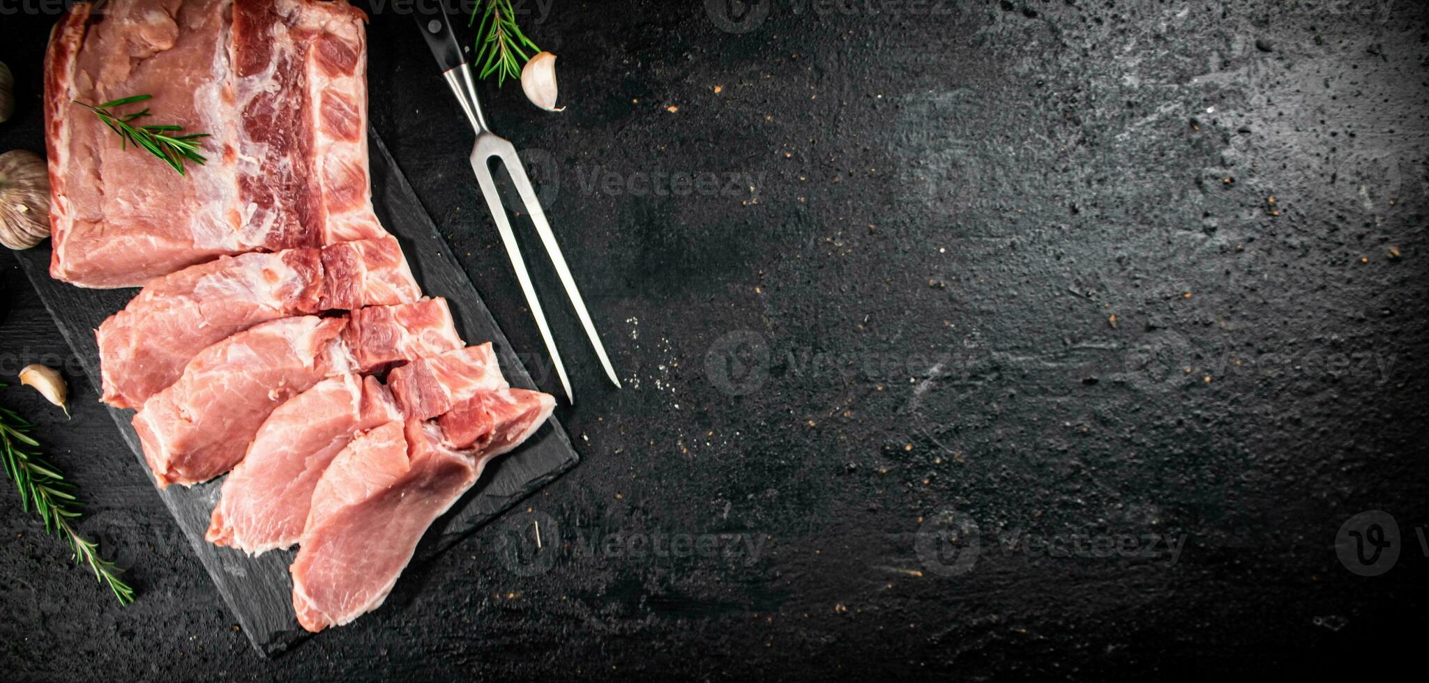 Chopped raw pork on a stone board with rosemary and garlic. photo