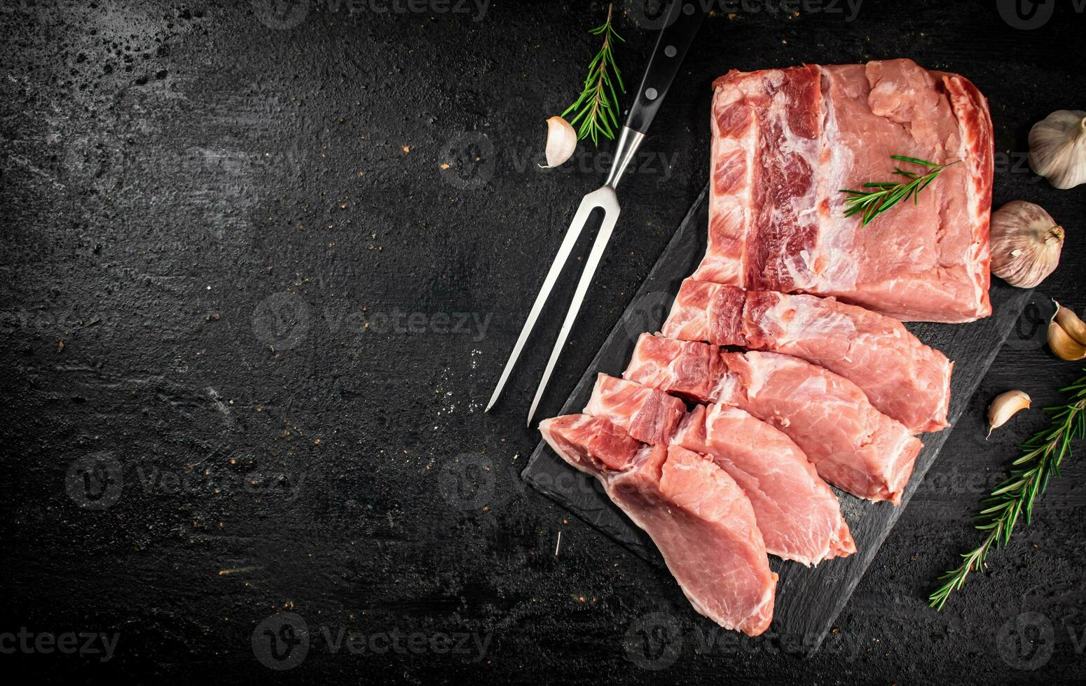 Chopped raw pork on a stone board with rosemary and garlic. photo