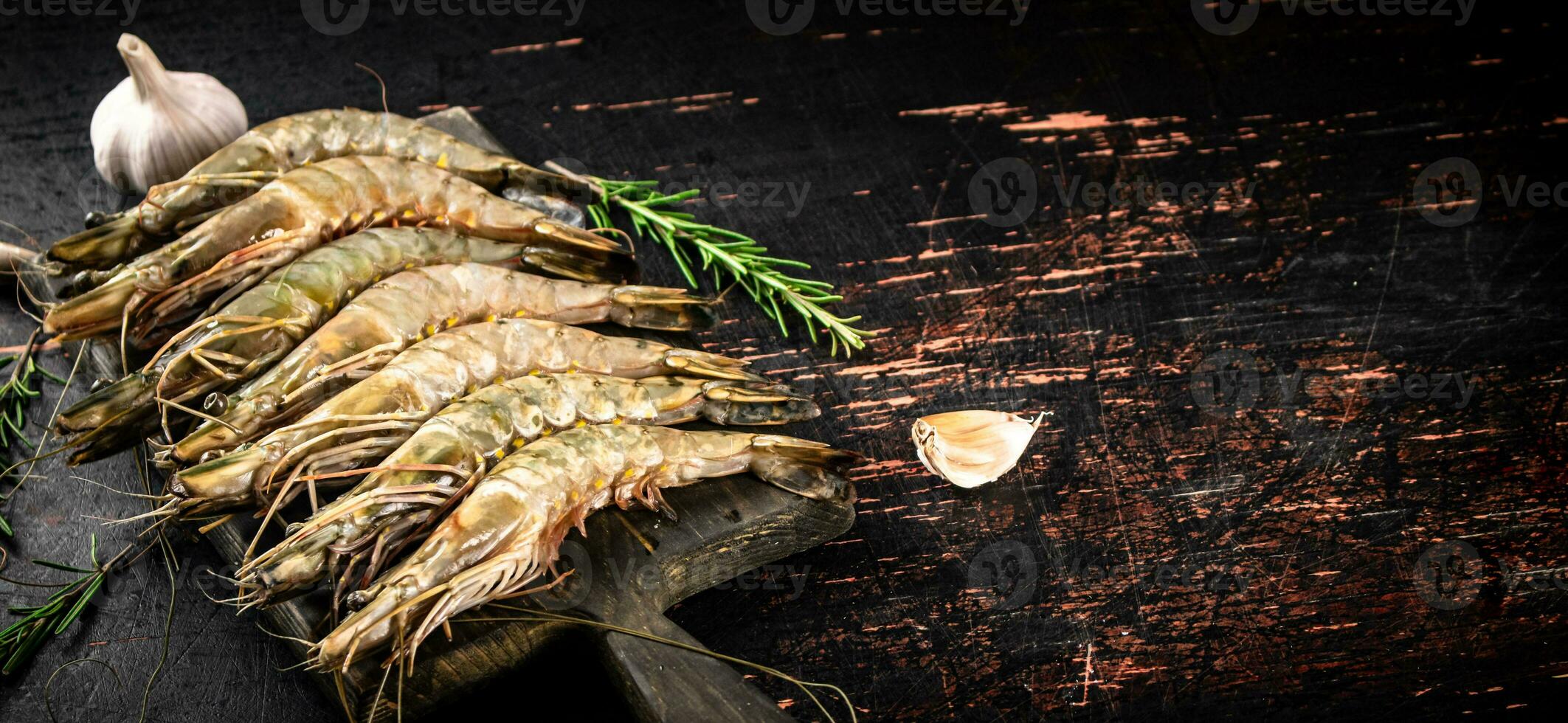 Raw shrimp on a cutting board with rosemary and garlic. photo