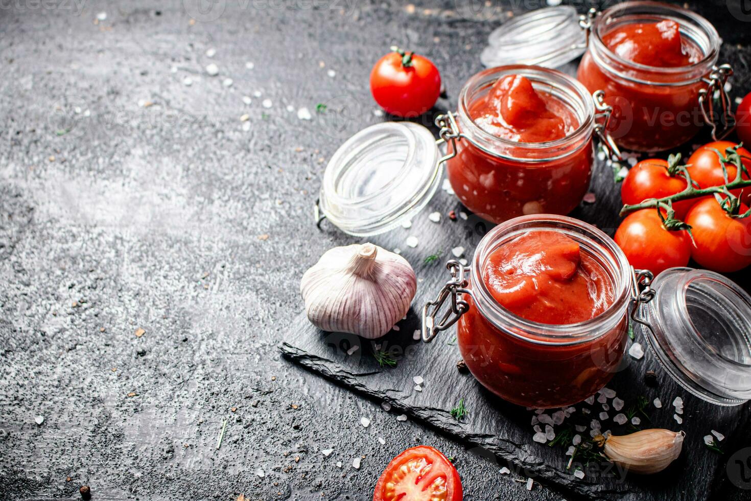 Tomato sauce in glass jars on a stone board with spices. photo