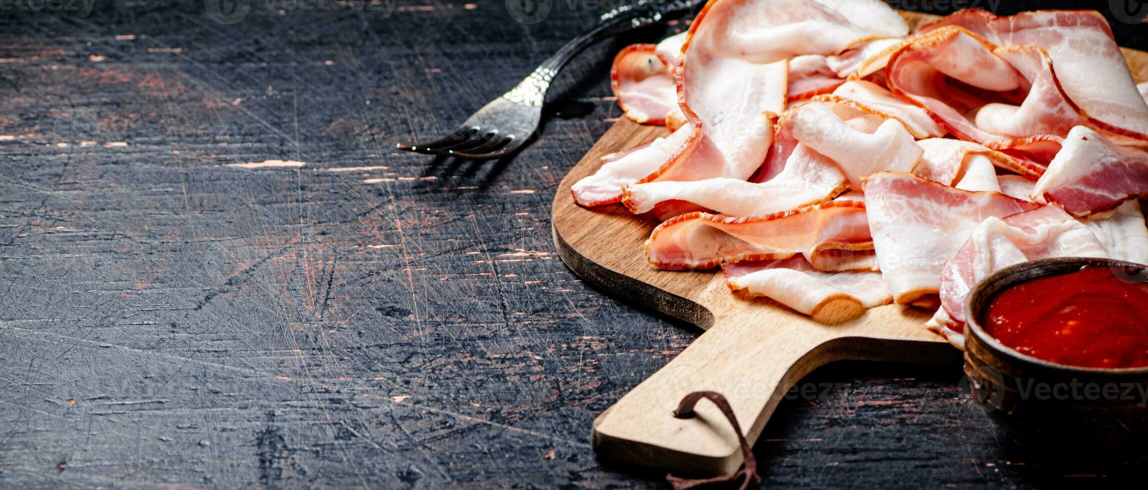 Pieces of bacon on a cutting board with tomato sauce. photo