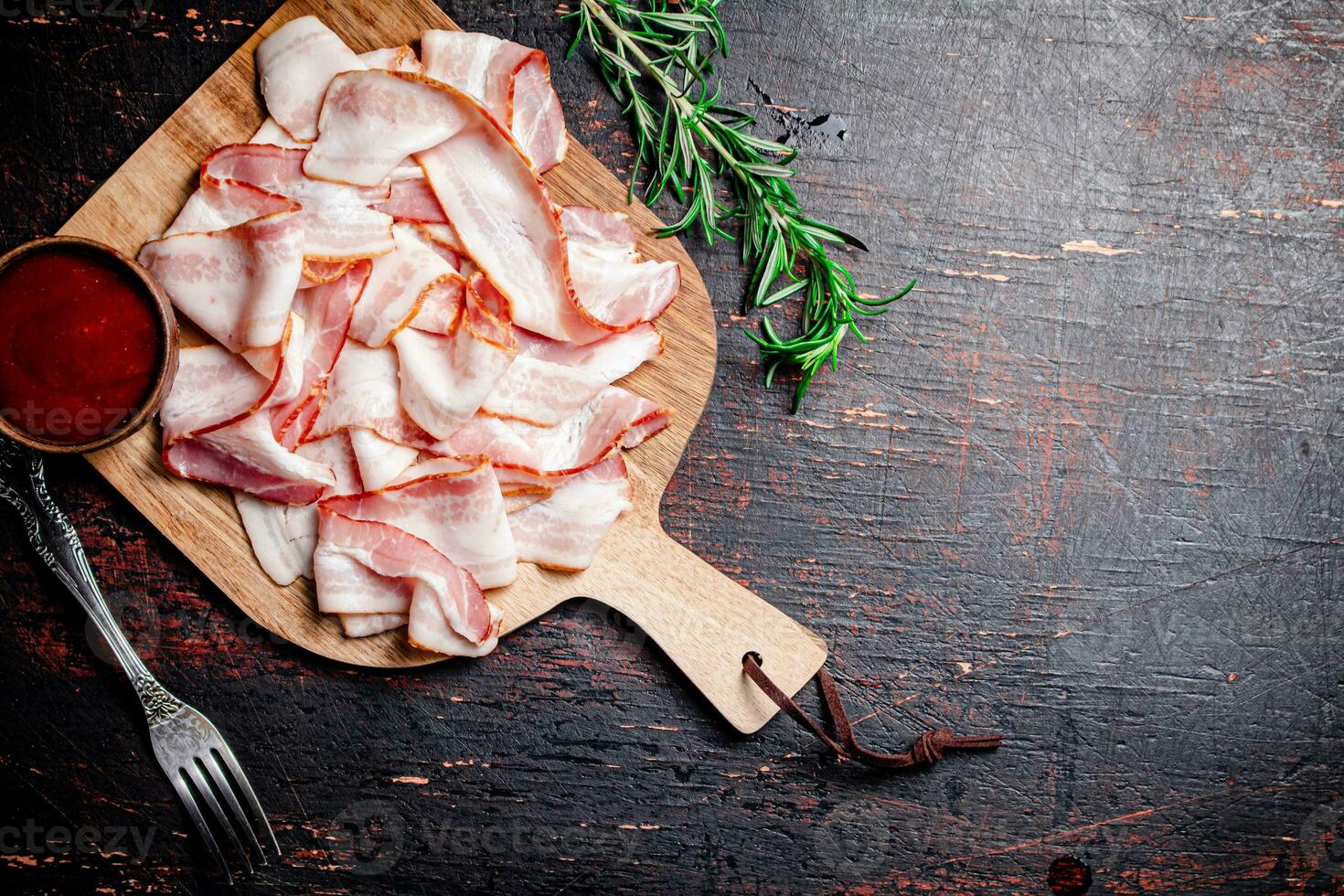 Pieces of bacon on a cutting board with tomato sauce. photo