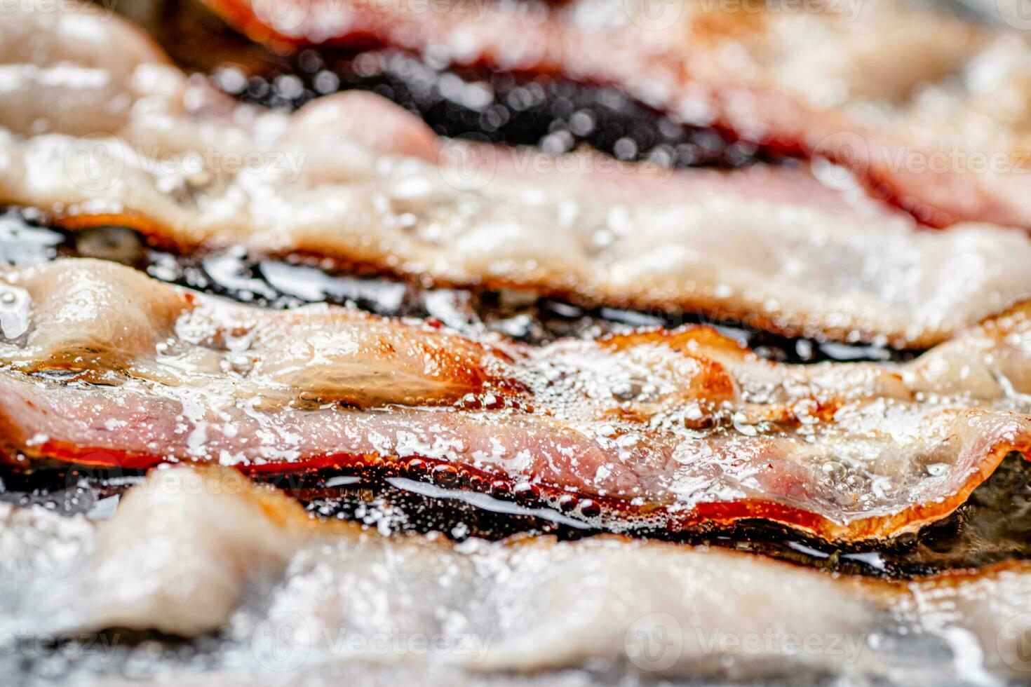 Pieces of bacon are fried in boiling oil with air bubbles. photo