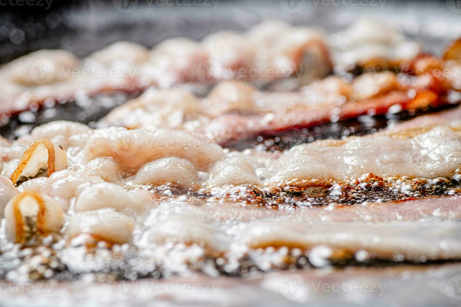 Pieces of bacon are fried in boiling oil with air bubbles. photo