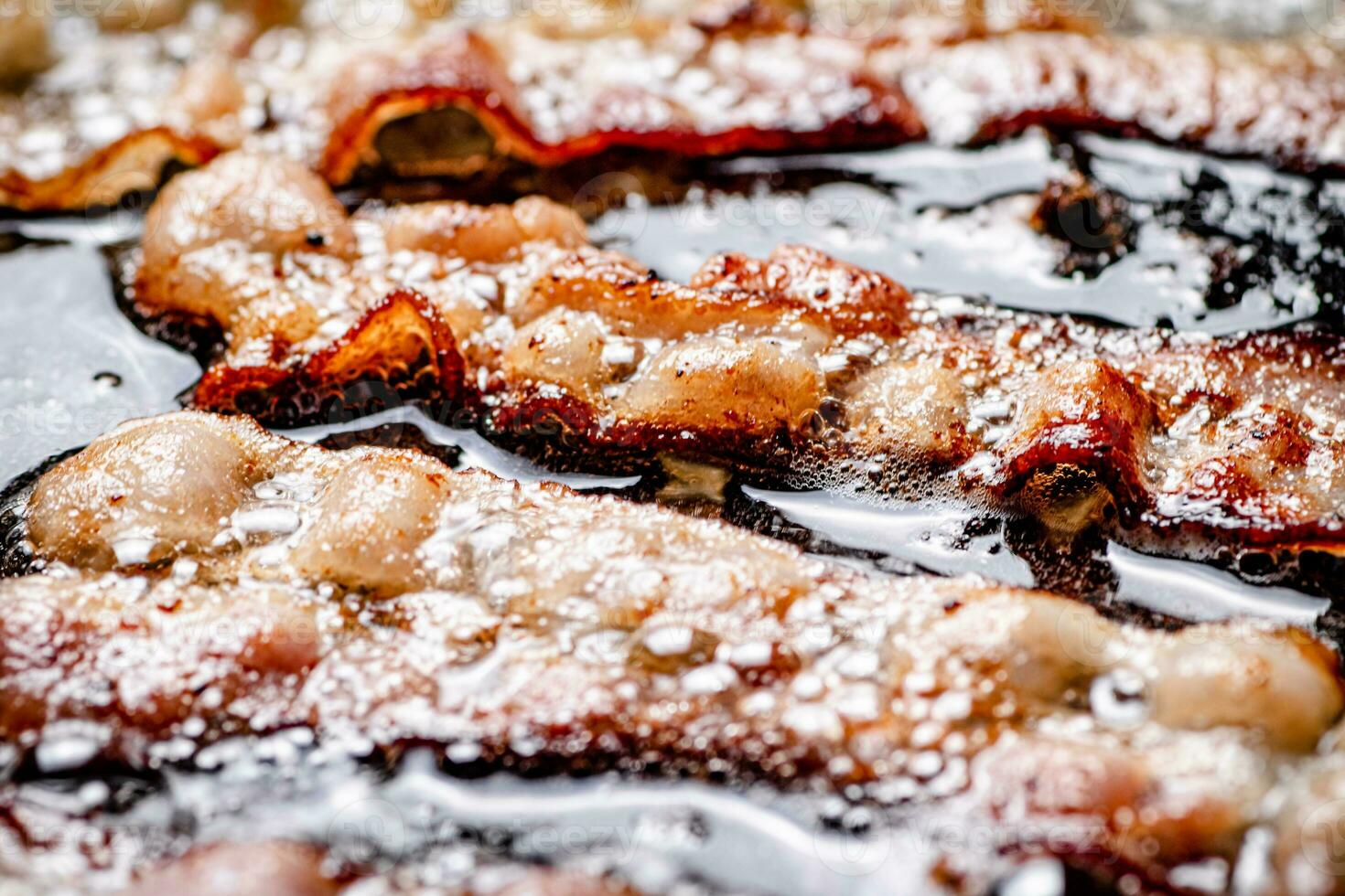 Pieces of bacon are fried in boiling oil with air bubbles. photo