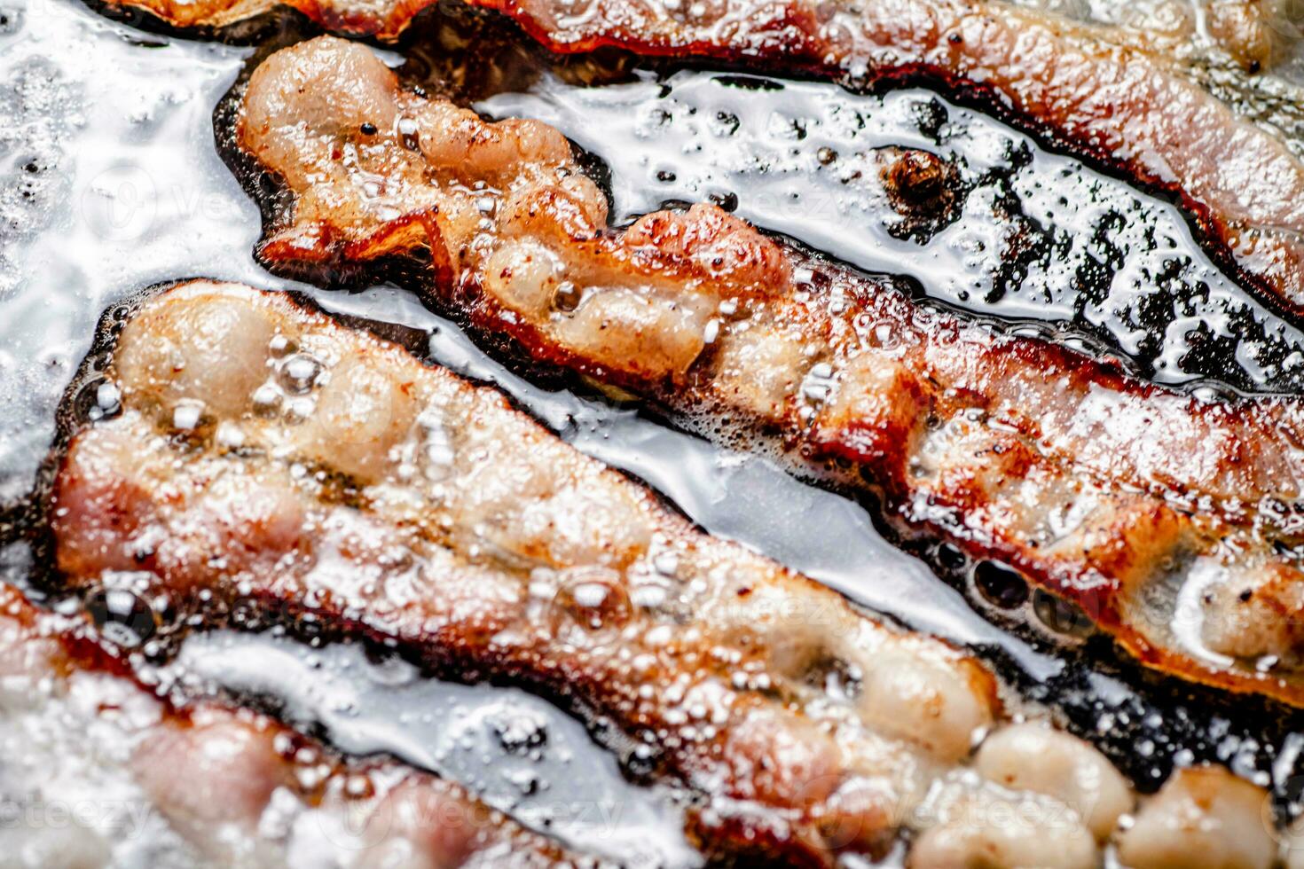 Pieces of bacon are fried in boiling oil with air bubbles. photo