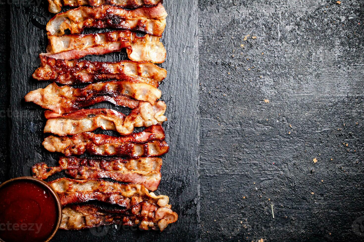 Strips of fried bacon on a stone board with tomato sauce. photo