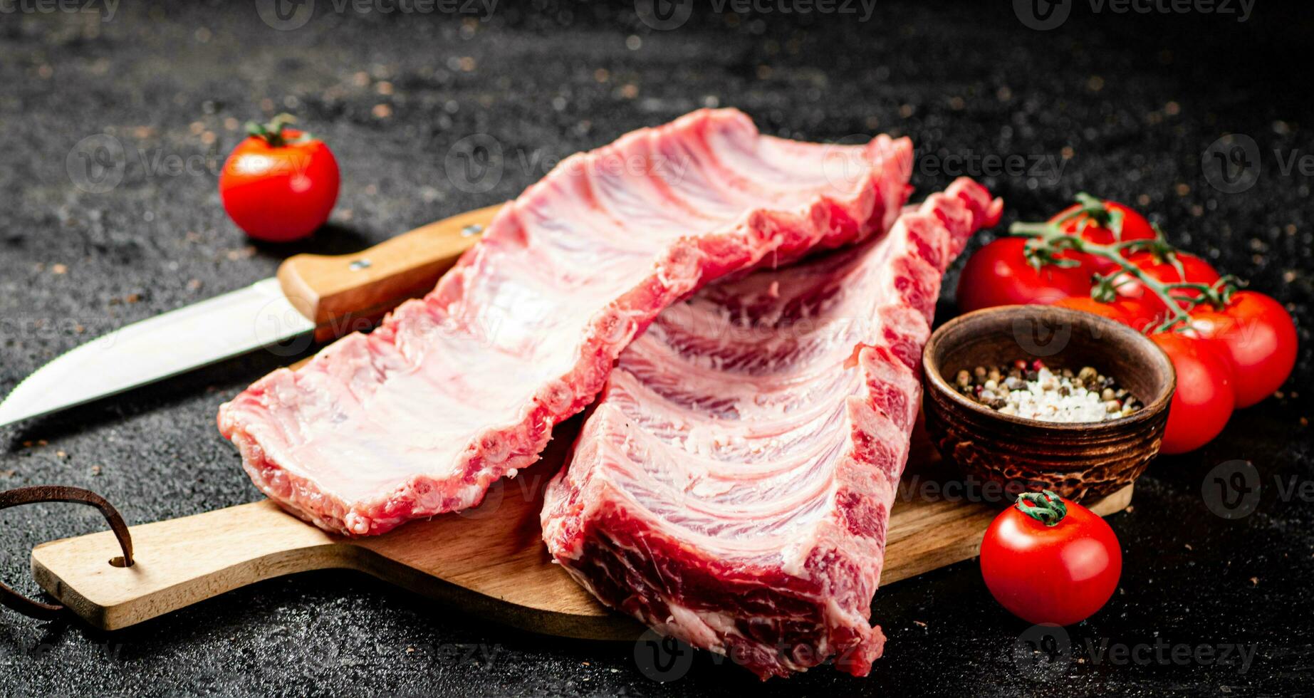 Raw ribs on a wooden cutting board with spices and tomatoes. photo