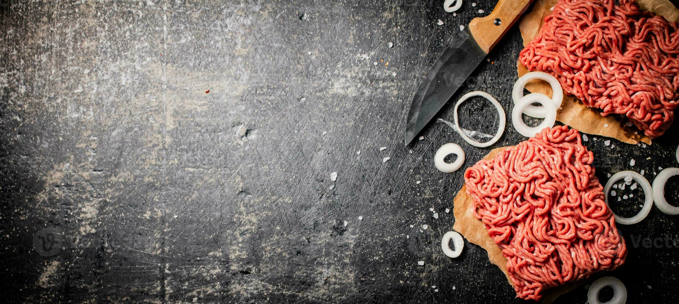 Fresh minced meat on paper on a table with a knife and onion rings. photo