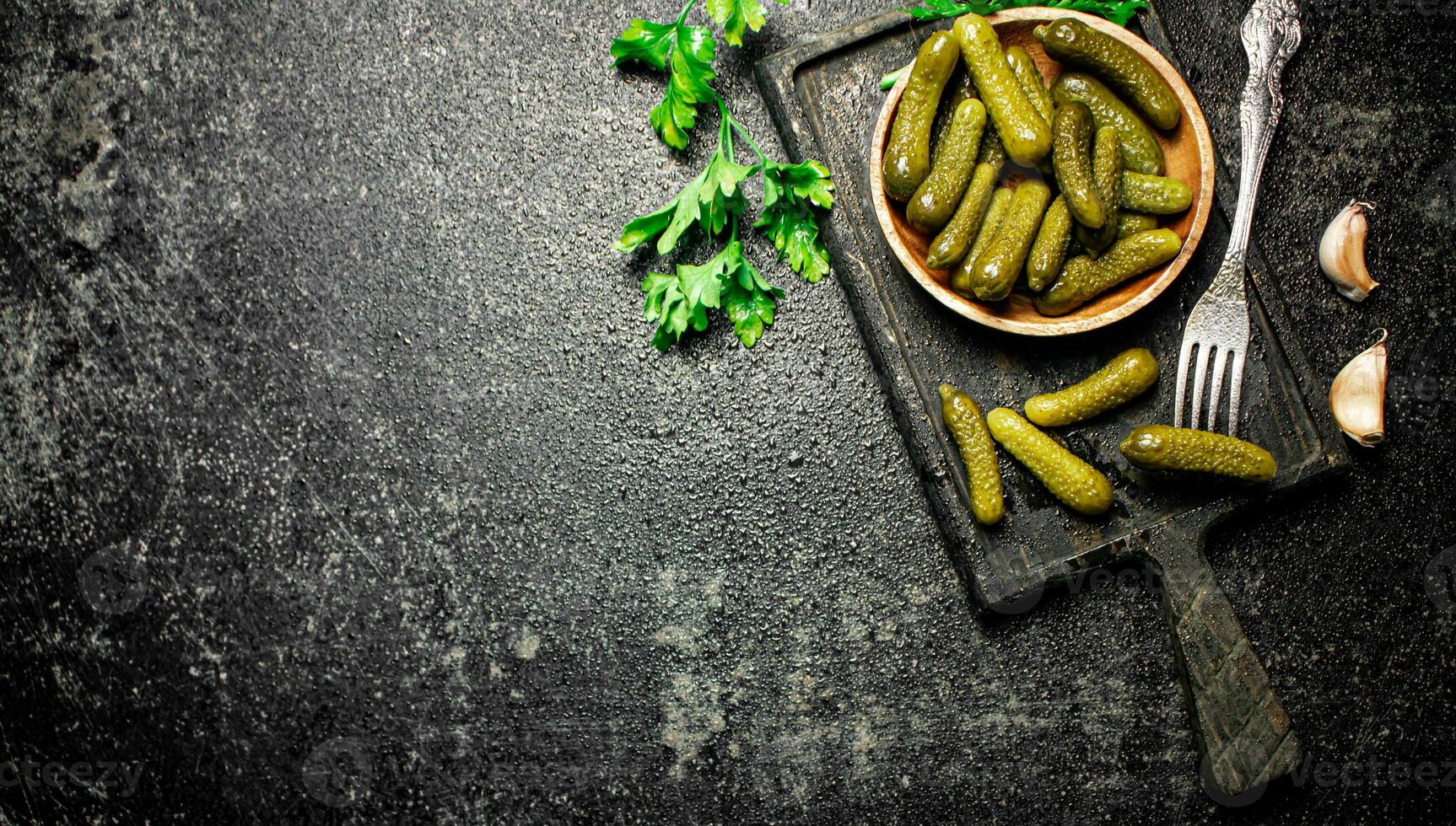 Wooden plate with pickles. On a black background. photo