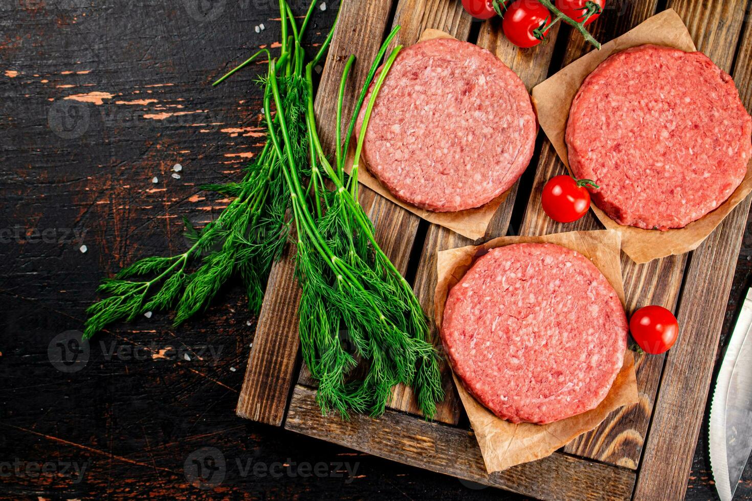 Raw burger on a wooden tray with tomatoes and dill. photo