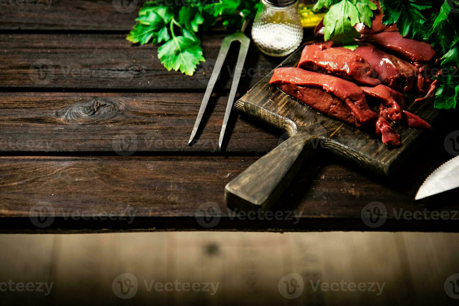 Pieces of raw liver on a cutting board with parsley and spices. photo