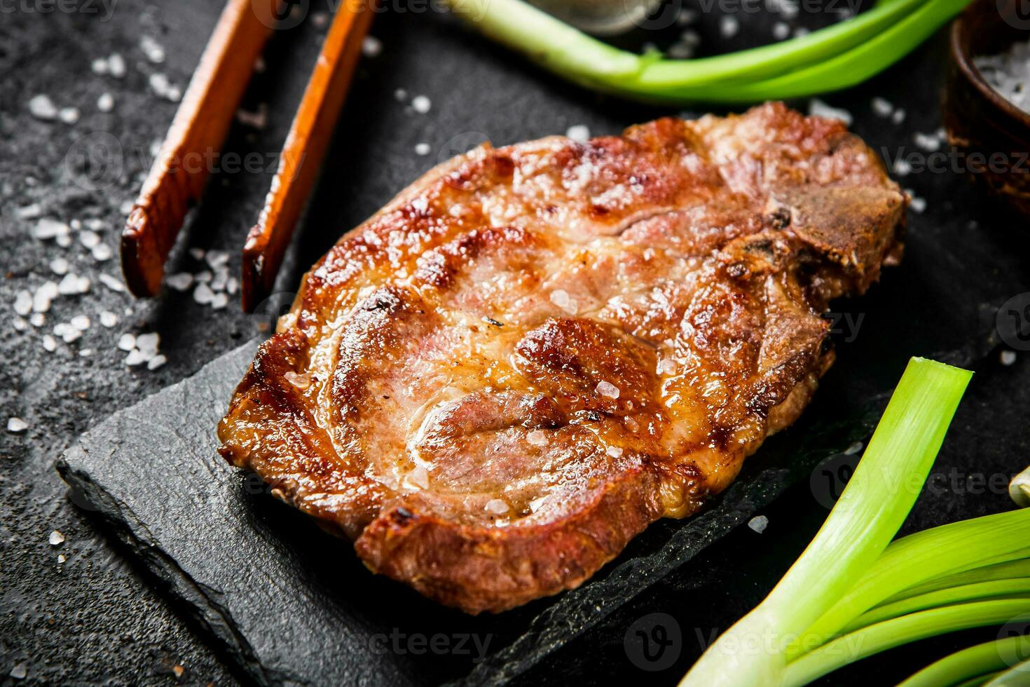 Grilled pork steak on a stone board with green onions and spices. photo