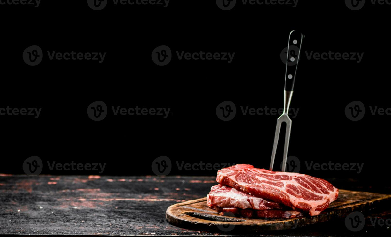 Raw pork steak on a cutting board with fork. photo