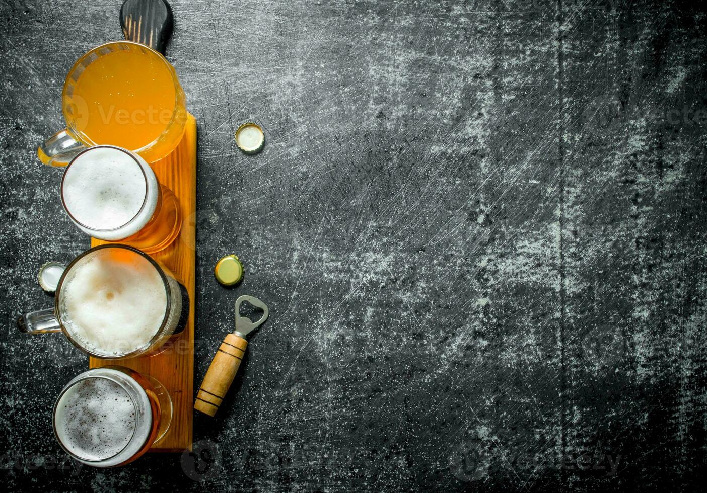 Different glasses of beer on a wooden cutting Board with opener. photo