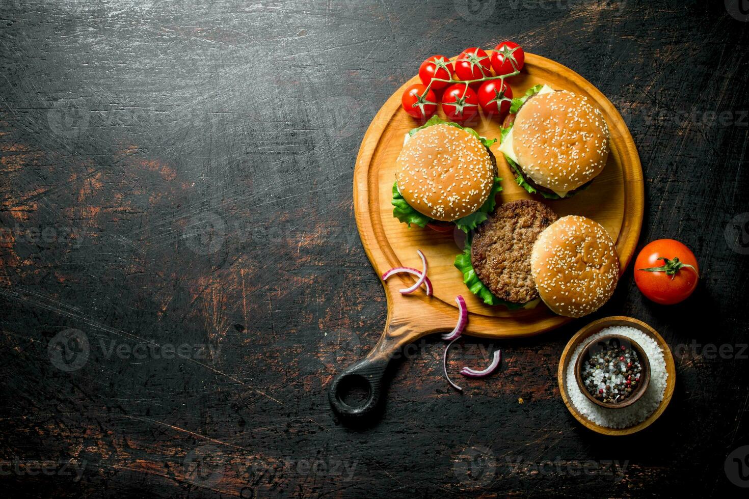 Burgers on a round cutting Board with spices and tomatoes. photo
