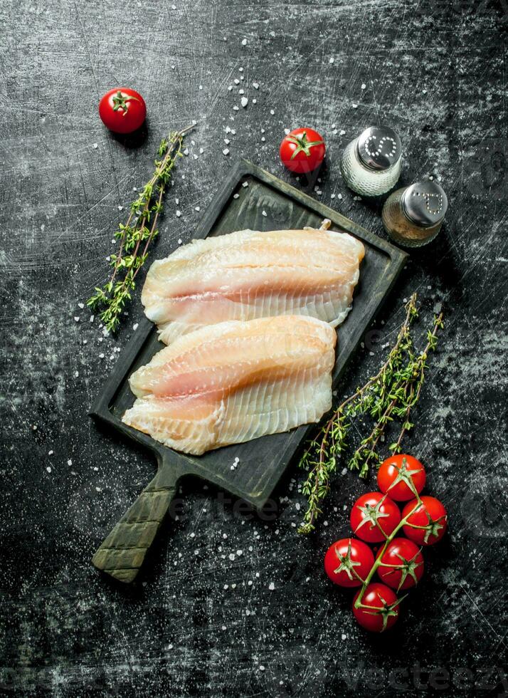 Fish fillet on a cutting Board with thyme, spices and tomatoes on a branch. photo