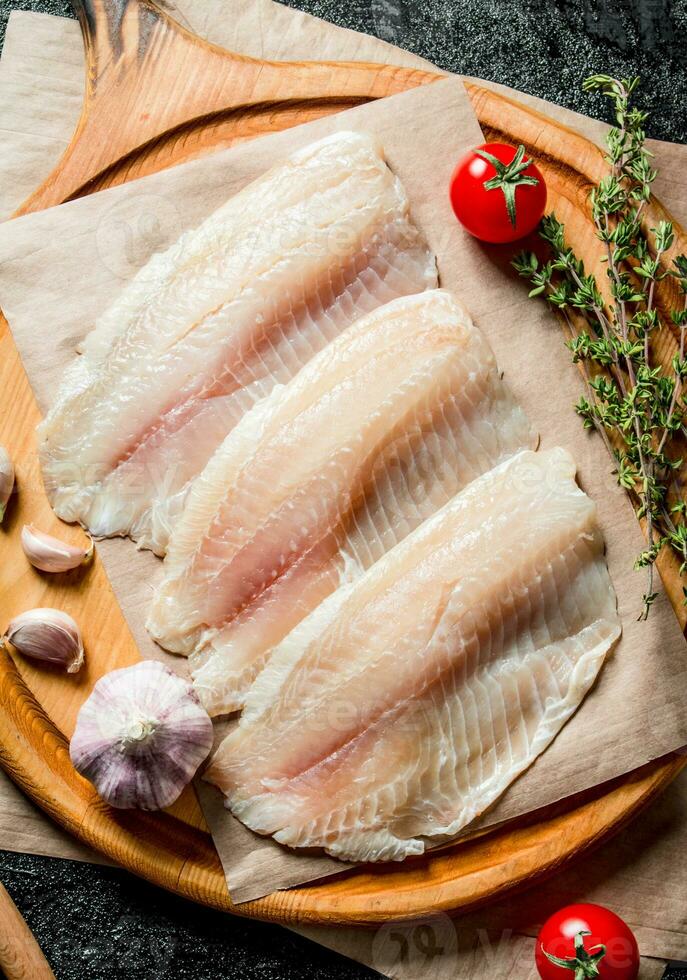 Tilapia fish fillet on a cutting Board with garlic cloves, tomatoes and thyme. photo