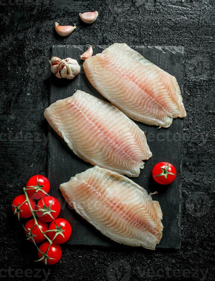 Fish fillet on a stone Board with cherry tomatoes and garlic. photo