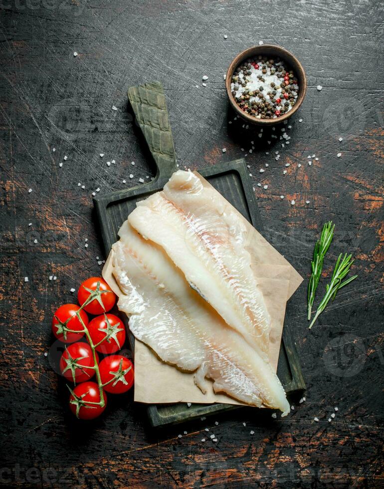 Fish fillets on the paper with a knife, rosemary and spices in a bowl. photo