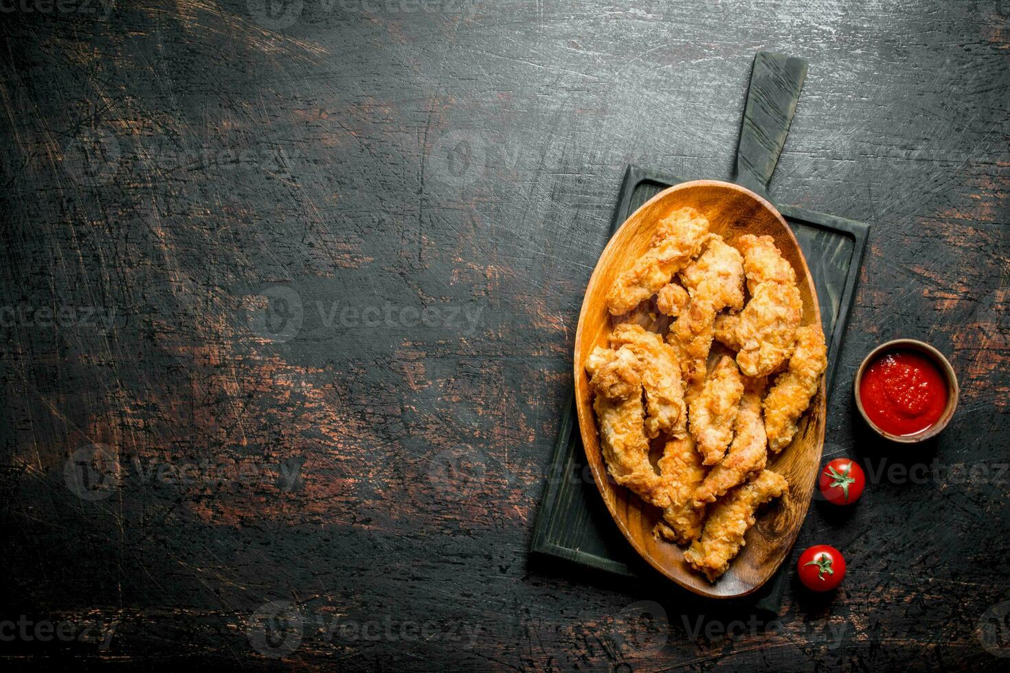 Chicken strips in a plate on a cutting Board with sauce and tomatoes. photo