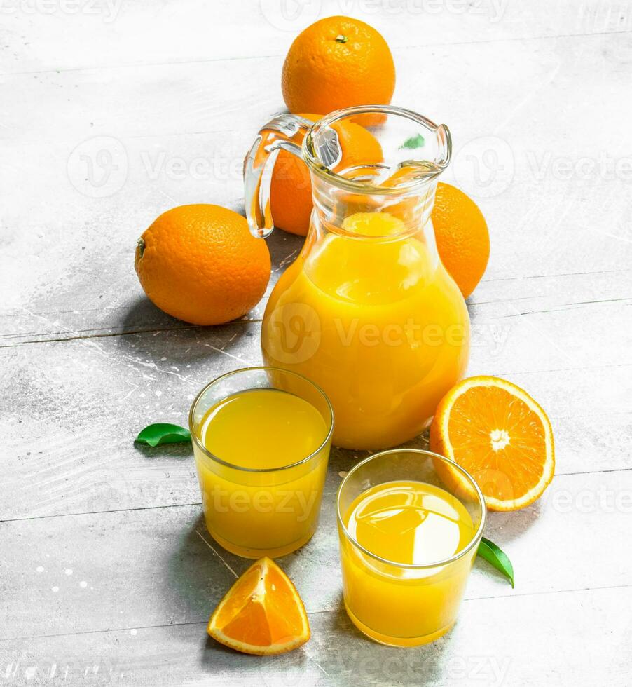 Orange juice in glass pitcher and fresh oranges. photo
