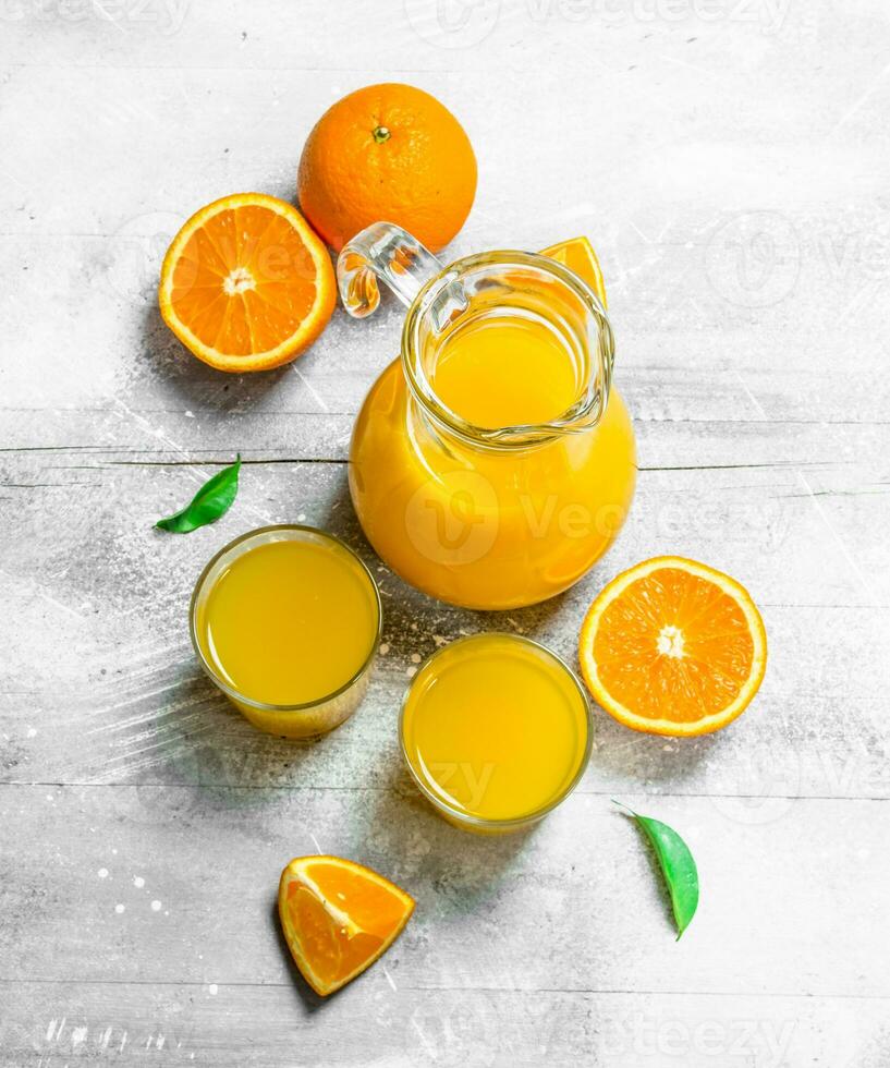 Orange juice in glass pitcher and fresh oranges. photo