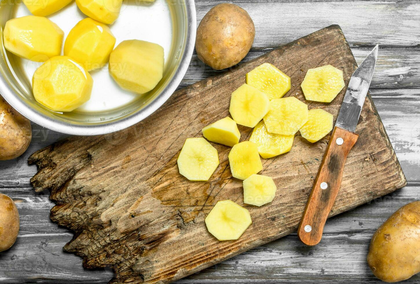 Sliced potatoes on a cutting Board with a knife and peeled potatoes in a saucepan. photo