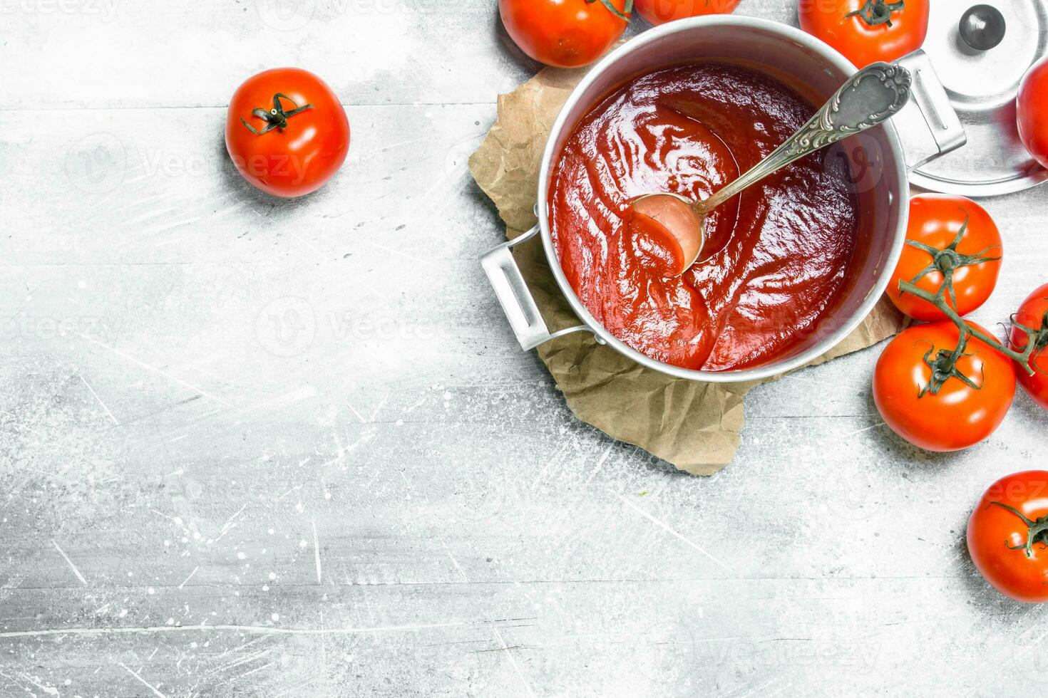 Tomato sauce in a pot with a spoon on paper and ripe tomatoes. photo