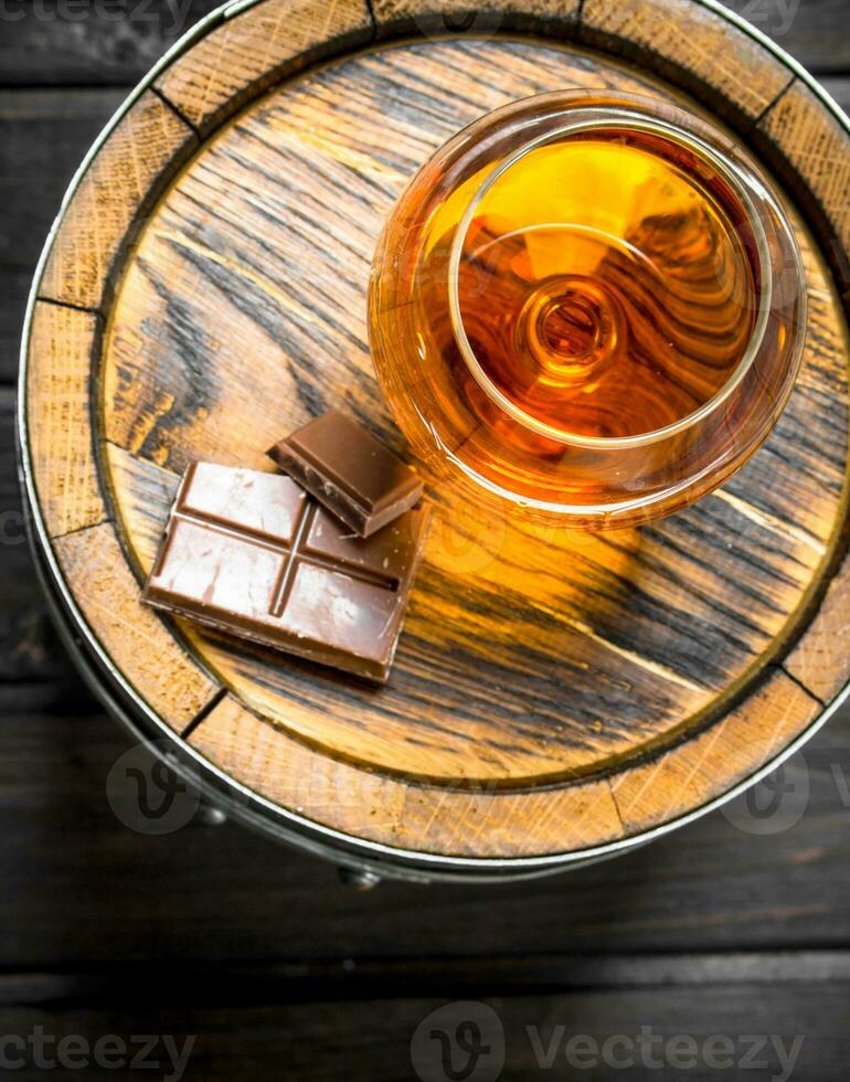 Cognac in a glass with chocolate on a barrel. photo