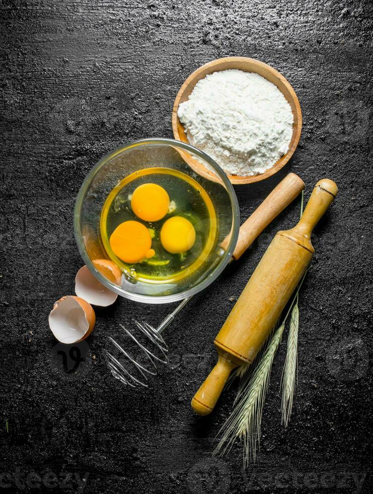 Flour with eggs, whisk and rolling pin. photo