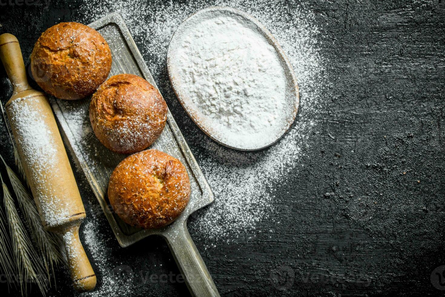 Crusty buns on a cutting Board with flour from the bowl. photo