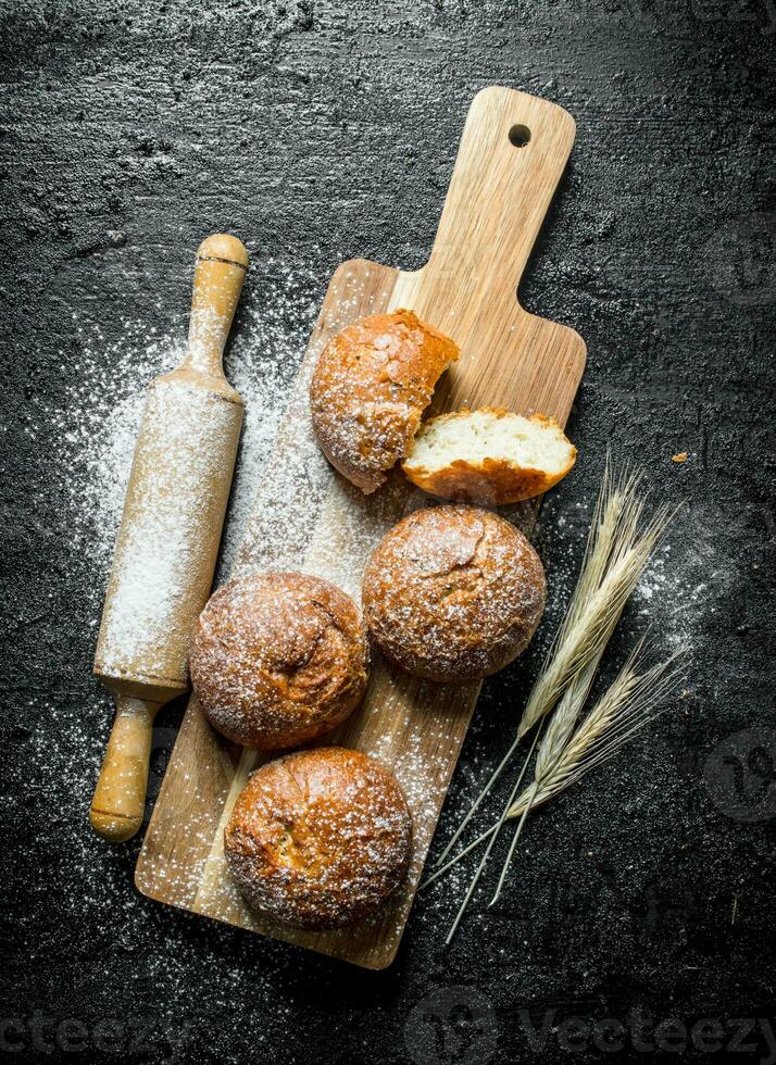 Fresh buns on a wooden cutting Board with a rolling pin and spikelets. photo