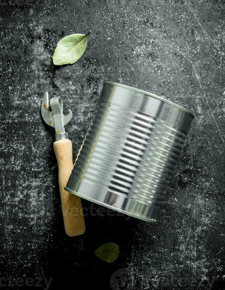 Closed tin can with a opener and a Bay leaf. photo