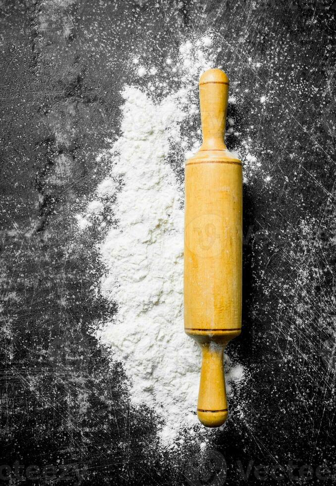 Wheat flour with rolling pin on rustic background. photo