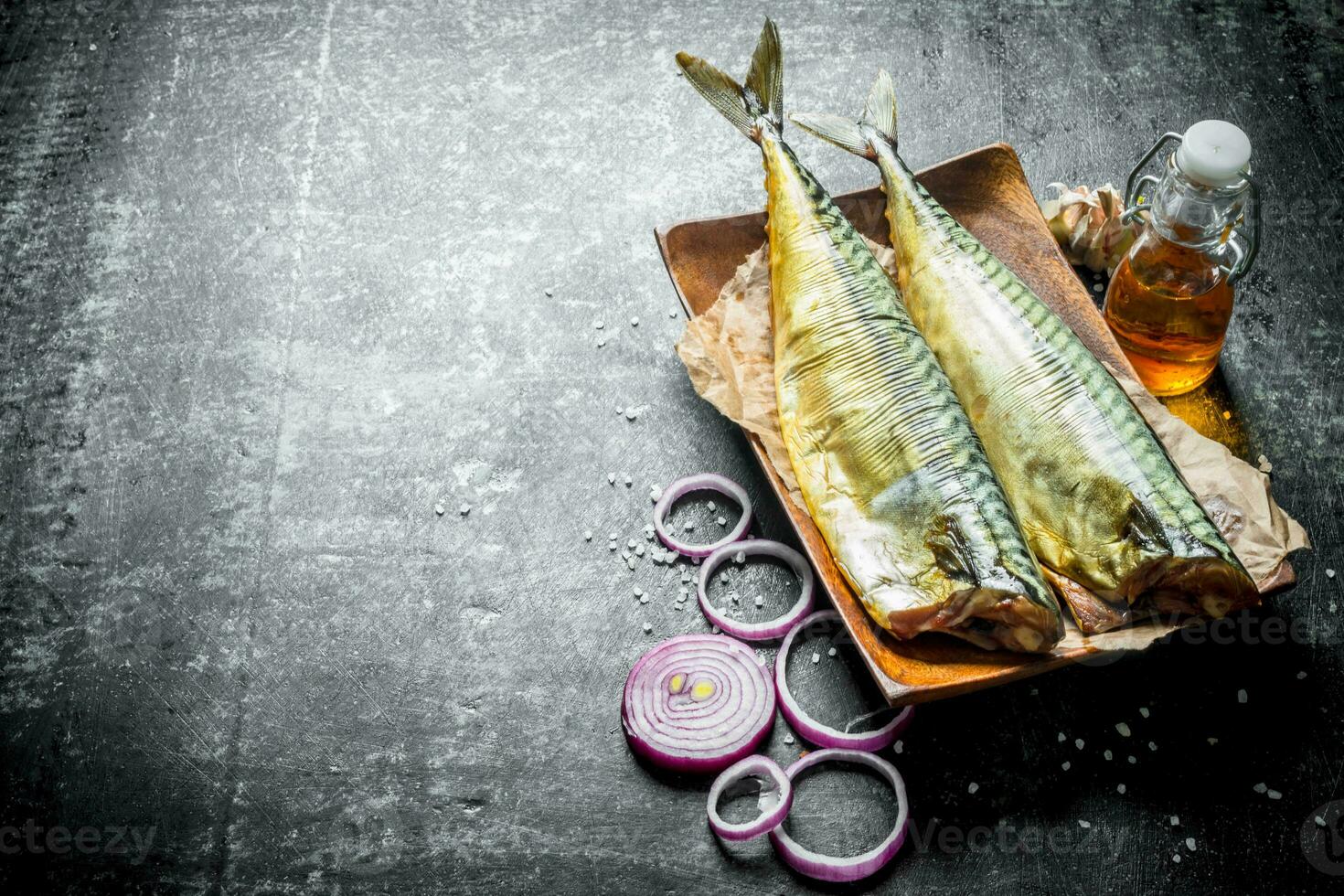 Smoked fish mackerel on a plate with onion rings and garlic. photo