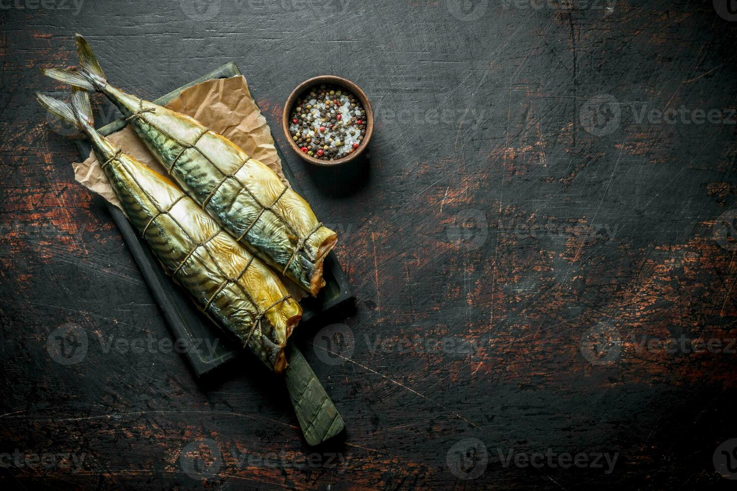 Appetizing smoked mackerel on paper with spices in bowl. photo